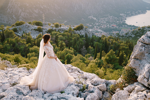The bride stands on top of a mountain with panoramic views of the Bay of Kotor, at sunset.