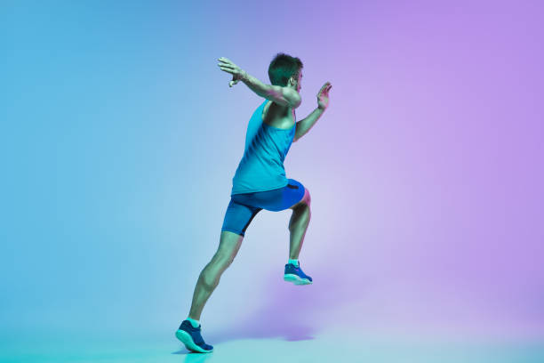 istock Full length portrait of active young caucasian running, jogging man on gradient studio background in neon light 1248721170