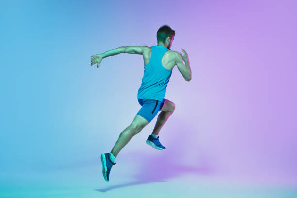 istock Full length portrait of active young caucasian running, jogging man on gradient studio background in neon light 1248721175