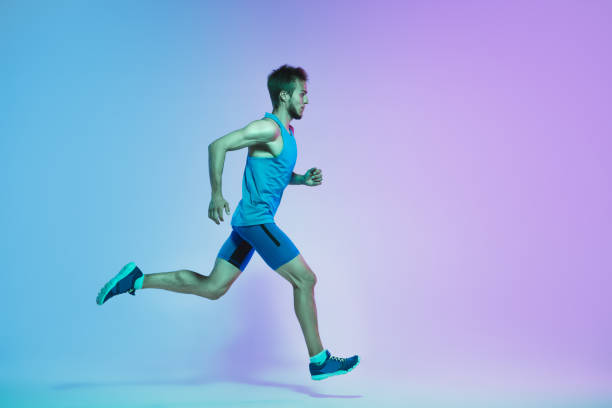 istock Full length portrait of active young caucasian running, jogging man on gradient studio background in neon light 1248721180