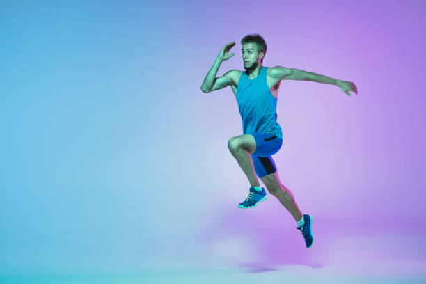 istock Full length portrait of active young caucasian running, jogging man on gradient studio background in neon light 1248721183