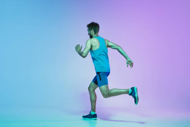 istock Full length portrait of active young caucasian running, jogging man on gradient studio background in neon light 1248721185