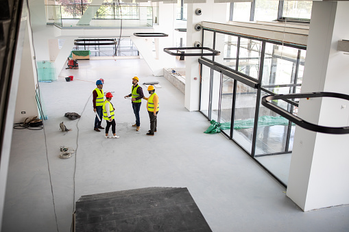 High angle view of construction engineers and architects wearing hardhats and safety vest, talking about work progress inside of nearly finished building