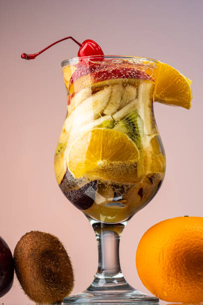 fruit salad of fresh fruits and berries in a transparent glass on a gradient background
