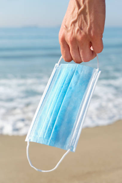istock man with a surgical mask in his hand on the beach 1248725979