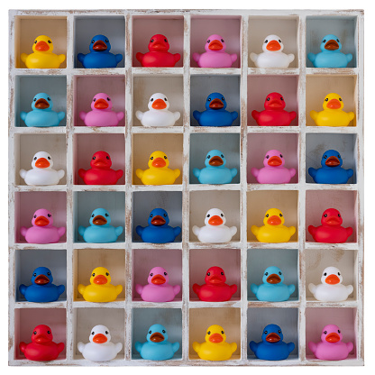 Many different colored rubber ducks sit in wooden pigeon hole compartments. Concept image regarding different ethnicity/gender people living together in harmony together in the same social environment, getting along together, living side by side.