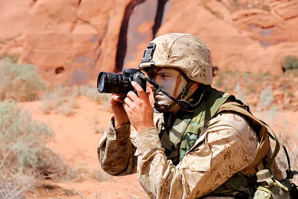 Marine In Desert Camouflage Uniform During Reconnaissance Mission. Red Sandstone Rock and Sand In Background.