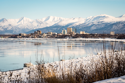 Scenic, panoramic view of downtown Anchorage from Point Woronzof Park while following Tony Knowles Coastal Trail. Reflection on Knik Arm. Covered with snow. Winter in Alaska. Snowy mountains.