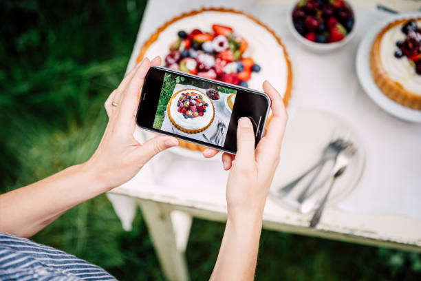 Woman photographing freshly made fruit cake Point of view of a woman taking photos of fresh berries cake with her mobile phone. Female photographing freshly made fruit cake outdoors. cream cheese photos stock pictures, royalty-free photos & images