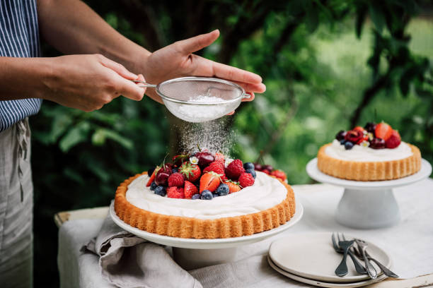 Woman preparing fresh fruits and berries cake Close-up of a woman hands sifting powdered sugar on a cheesecake. Female preparing fresh fruits and berries cake outdoors in a garden. sprinkling powdered sugar stock pictures, royalty-free photos & images