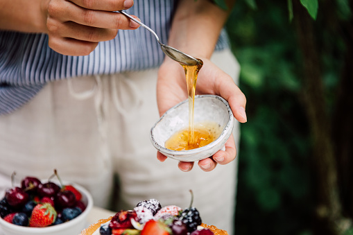 Close-up of a woman preparing cake for breakfast outdoors in the garden. Female making cheesecake, adding honey on the cake.