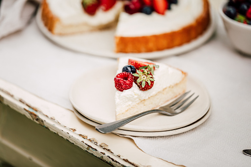 Close-up of a freshly made fruit cake slice served in a plate on a table. Homemade cheesecake with berries.