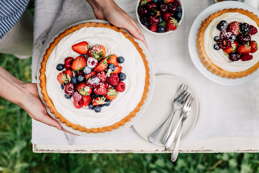 Top view of a woman placing fruit cake on table. Female setting cake table outdoors in garden for afternoon snack.