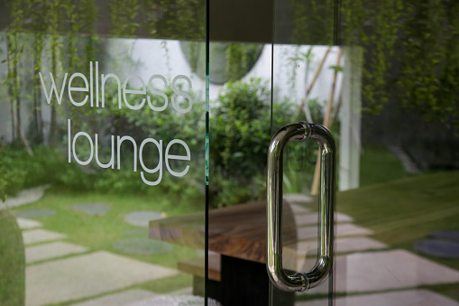 Wellness lounge beauty salon sign on the glass door with greenery reflexion