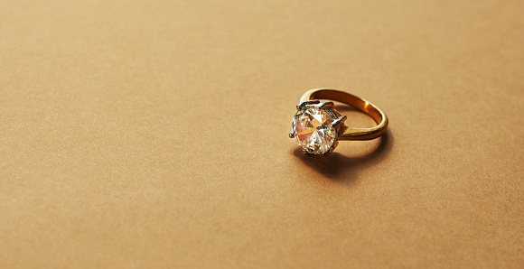 Studio shot of a gold ring with a diamond against a brown background