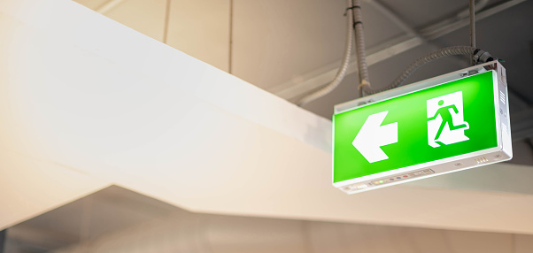 The Large bright green fire exit lights hanging in the building for show the way to escape due to the being fire in the building or public area.