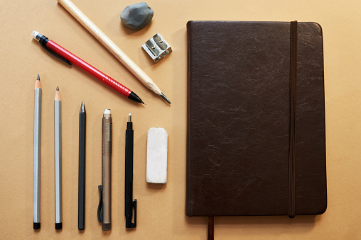 Studio shot of a sketchpad and other various artistic against a brown background