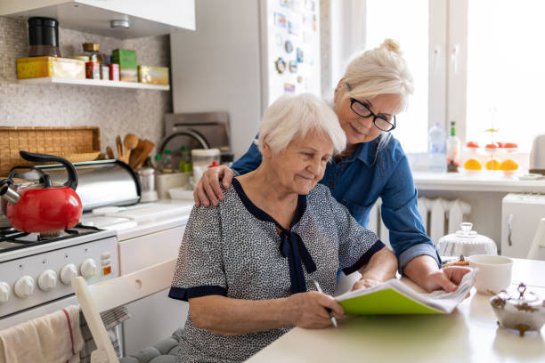 donna matura che aiuta la madre anziana con le scartoffie - grandparent senior adult child reading foto e immagini stock