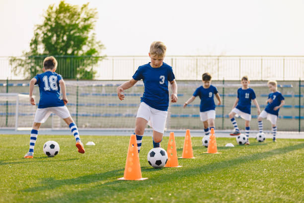 サッカートレーニング - ウォームアップとスラロームドリル。芝生のフィールドでヨーロッパサッカーを練習する少年たち - 子供サッカー ストックフォトと画像