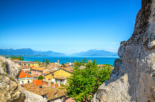 View of historical centre Desenzano del Garda old town, lake and mountain range through merlons of brick stone ruined wall of medieval castle, blue sky copy space, Lombardy, Northern Italy