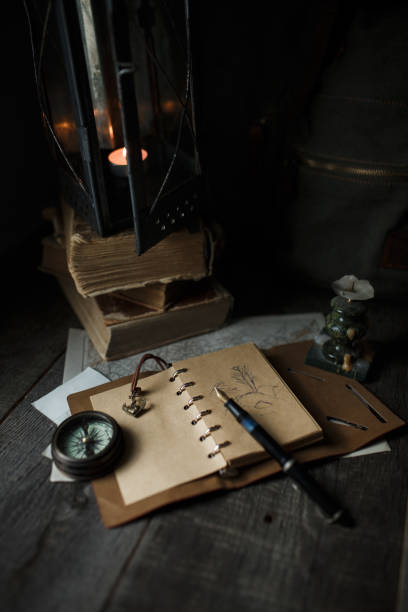 istock Old lamp and books lying on the table. A flame from an old source of light illuminating old prints. Black wooden background 1248742771