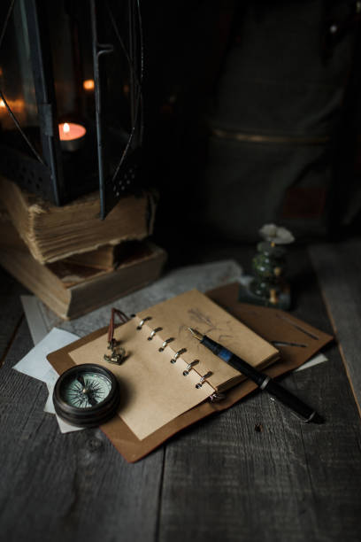 istock Old lamp and books lying on the table. A flame from an old source of light illuminating old prints. Black wooden background 1248742900