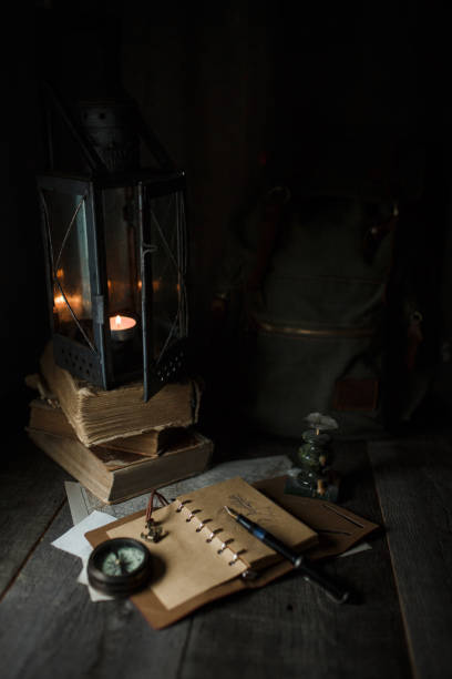 istock Old lamp and books lying on the table. A flame from an old source of light illuminating old prints. Black wooden background 1248743012