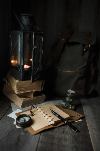 istock Old lamp and books lying on the table. A flame from an old source of light illuminating old prints. Black wooden background 1248743127