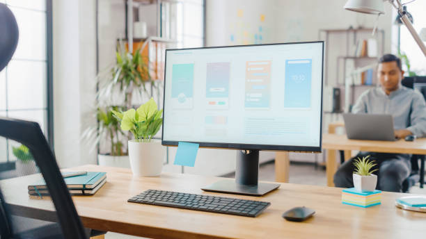 istock Desktop Computer Standing on the Desk in the Modern Creative Office. Screen Showing Smartphone Application UI / UX.  In the Background Bright Studio with Young Professionals Work on Computers. 1248743221