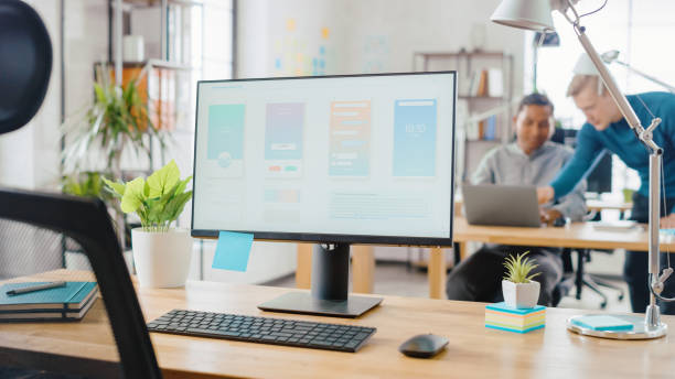 istock Desktop Computer Standing on the Desk in the Modern Creative Office. Screen Showing Smartphone Application UI / UX.  In the Background Bright Studio with Team of Young Professionals Work on Computers. 1248743226