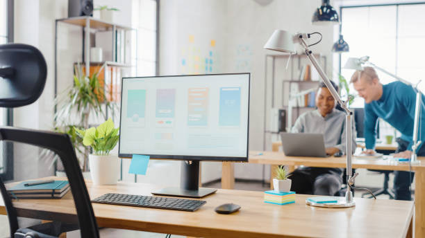 istock Desktop Computer Standing on the Desk in the Modern Creative Office. Screen Showing Smartphone Application UI / UX.  In the Background Bright Studio with Team of Young Professionals Work on Computers. 1248743242