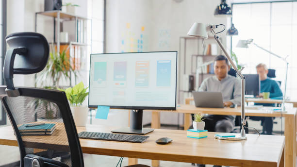 istock Desktop Computer Standing on the Desk in the Modern Creative Office. Screen Showing Smartphone Application UI / UX.  In the Background Bright Studio with Team of Young Professionals Work on Computers. 1248743244