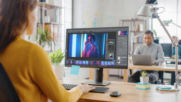 istock Over the Shoulder: Creative Young Woman Digital Editor Works in Photo Editing Software on Her Personal Computer with Big Display. In the Background Loft Office with Diverse Team of Young Professionals 1248743272