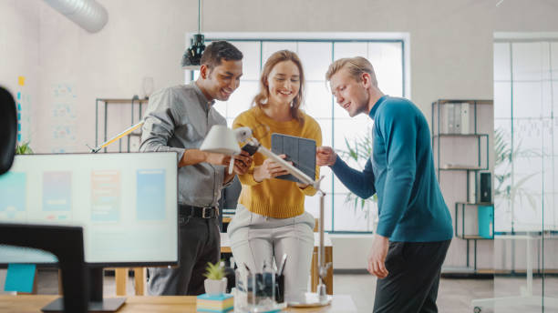 istock In the Office: Three Diverse Start-up Entrepreneurs Have Meeting and Discussion about the Project. Share Touch Screen Digital Tablet and Smartphone Screens.Young Professionals Smile and Joke Around. 1248743382