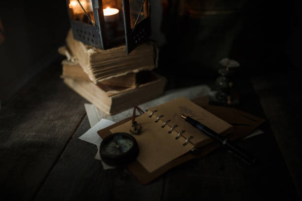 istock Old lamp and books lying on the table. A flame from an old source of light illuminating old prints. Black wooden background 1248743395