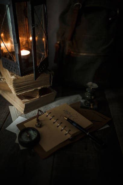 istock Old lamp and books lying on the table. A flame from an old source of light illuminating old prints. Black wooden background 1248743832