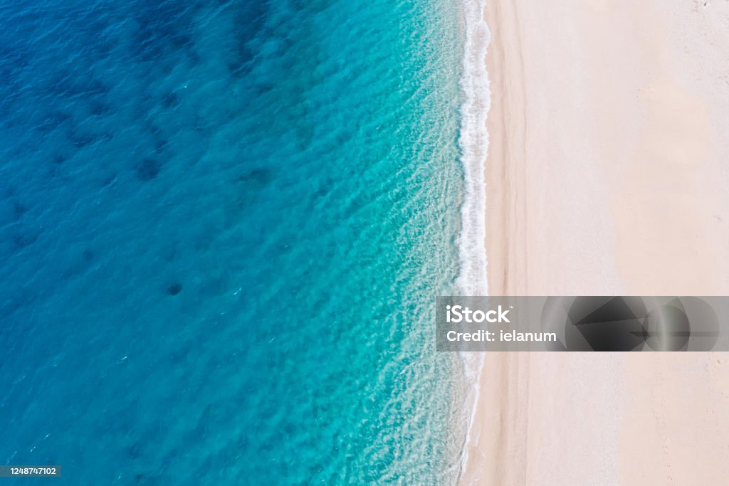 Top-down aerial view of a white sandy beach on the shores of a beautiful turquoise sea. Top-down aerial view of a clean white sandy beach on the shores of a beautiful turquoise sea. Greece. Beach Stock Photo