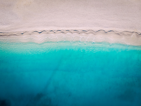 Top-down aerial view of a clean white sandy beach on the shores of a beautiful turquoise sea. Greece.