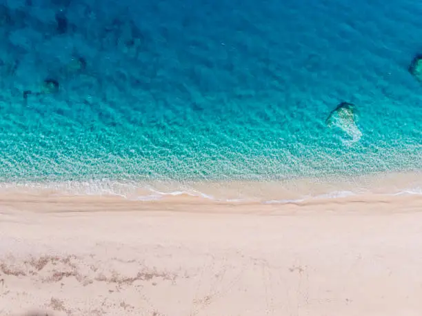 Top-down aerial view of a clean white sandy beach on the shores of a beautiful turquoise sea. Greece.