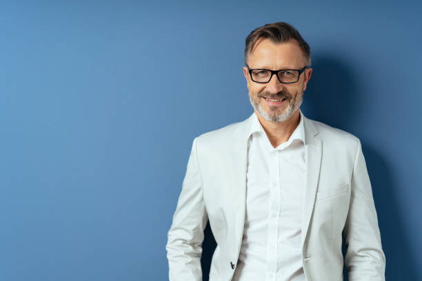 Smiling middle age man in glasses on blue Half-length portrait of smiling handsome middle-aged man in glasses and white blazer on blue background with copy space blazer jacket photos stock pictures, royalty-free photos & images