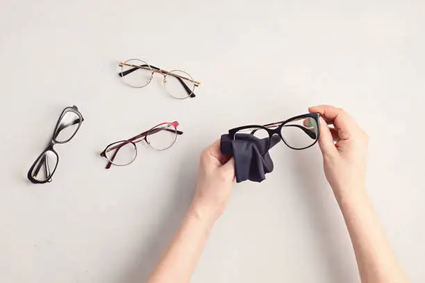 Photo of Woman hand cleaning eyeglasses. Optical store, glasses selection, eye test, vision examination at optician, fashion accessories concept. Top view