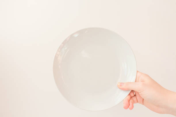 istock Female hand holds a white round plate on a white background as a mockup with copy space. Ceramic flat saucer 1248753197