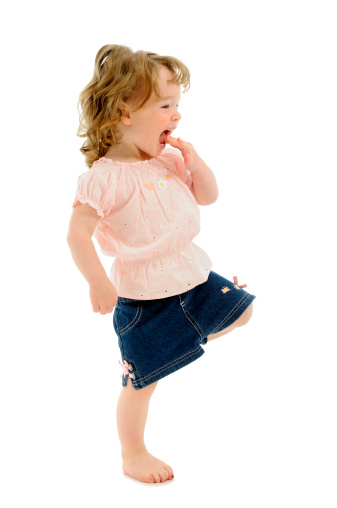 Little Girl Hopping On One Foot & Laughing In Delight, Isolated on White.