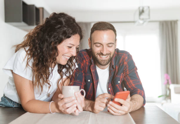 giovane coppia ride mentre usa lo smartphone - coppia innamorata a fare colazione insieme e leggere le ultime notizie usando il telefono cellulare - coffee couple italy drinking foto e immagini stock