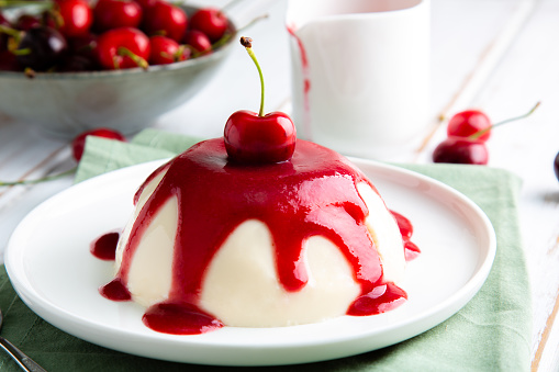 Italian panna cotta dessert with cherry coulis on a white wooden table