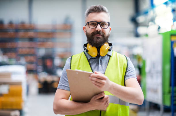 Technician or engineer with protective headphones standing in industrial factory. Technician or engineer with protective headphones standing in industrial factory, looking at camera. one mature man only audio stock pictures, royalty-free photos & images