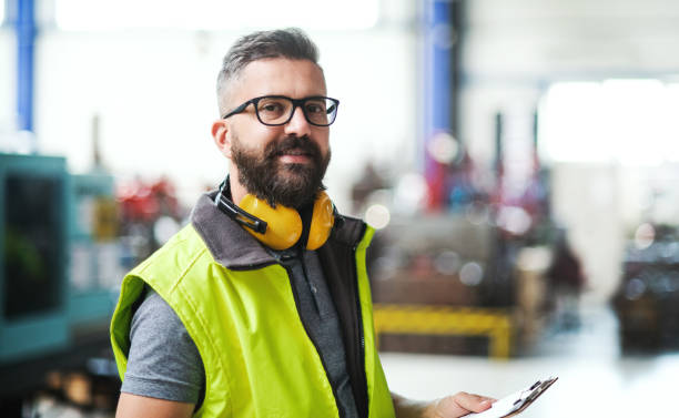 Technician or engineer with protective headphones standing in industrial factory.