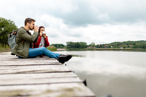 Adorable young adventurous couple sitting on the wooden pier at the lake, relaxing, enjoying the moment