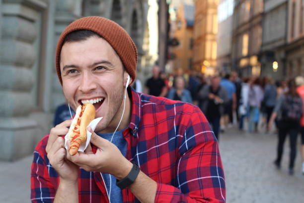 junger mann isst einen hot dog im freien - people eating walking fun stock-fotos und bilder