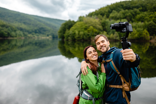 Charming young travel couple, exploring the beautiful nature near lake, and recording their experience for their travel vlog on social media